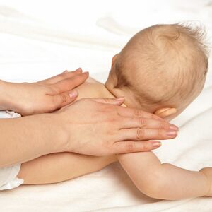 Eine Mutter massiert mit den Händen den Rücken ihres Babys.