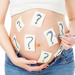 Am Bauch einer hochschwangeren Frau hänge viele Klebezettel mit Fragezeichen drauf.